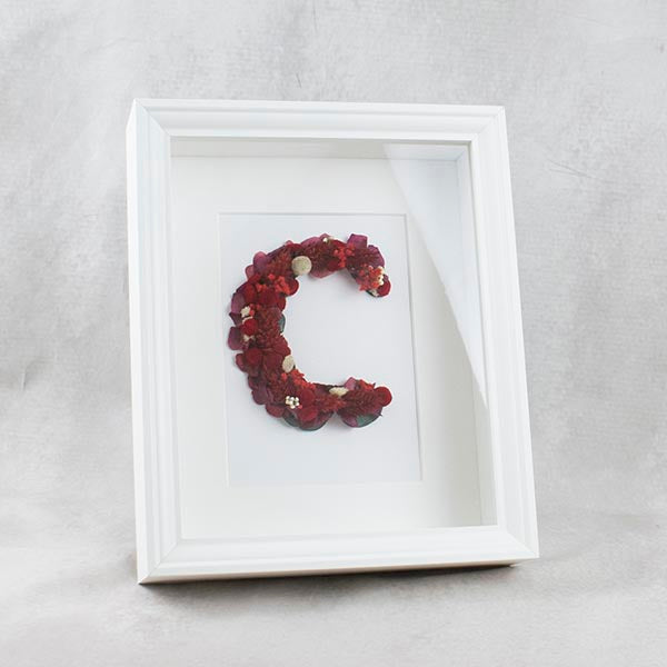 marco con una inicial hecha con flores en tonos rojos